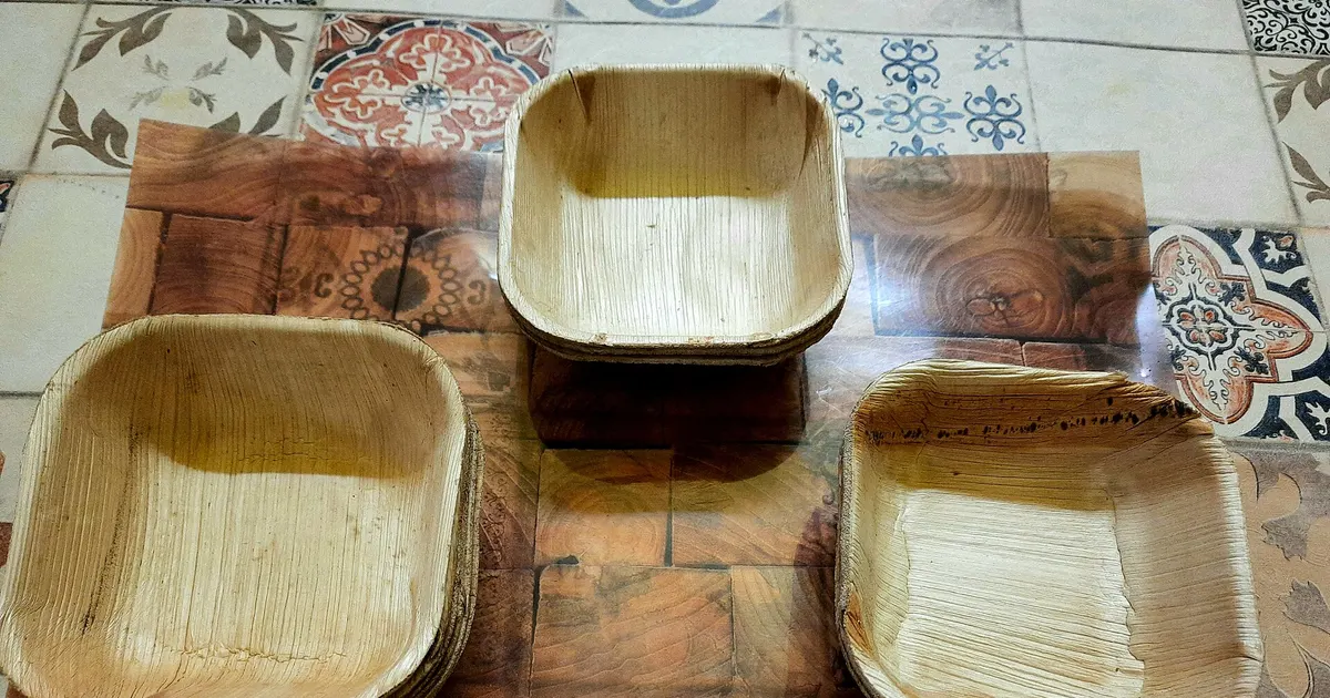 Square areca palm leaf plates stacked on a tiled floor, showing the natural grain that areca leaf plates grades are based on