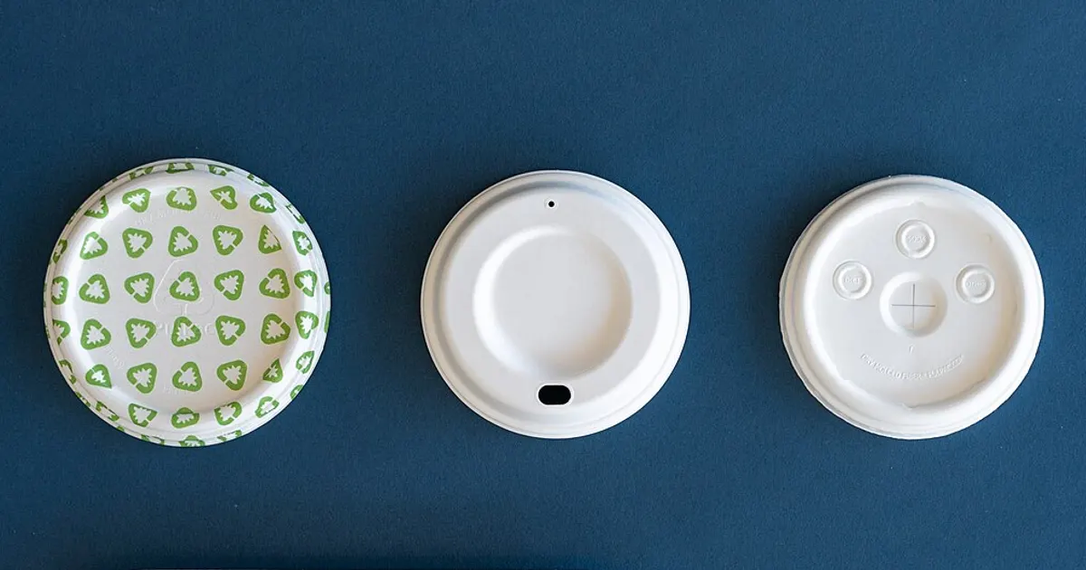 Two white molded fiber cup lids, one with a sip opening, next to a printed paper plate on a blue background